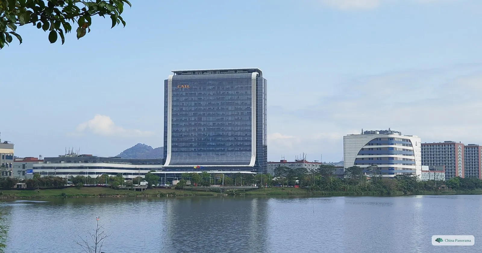 A tall glass tower with the letters CATL near the top across a calm lake