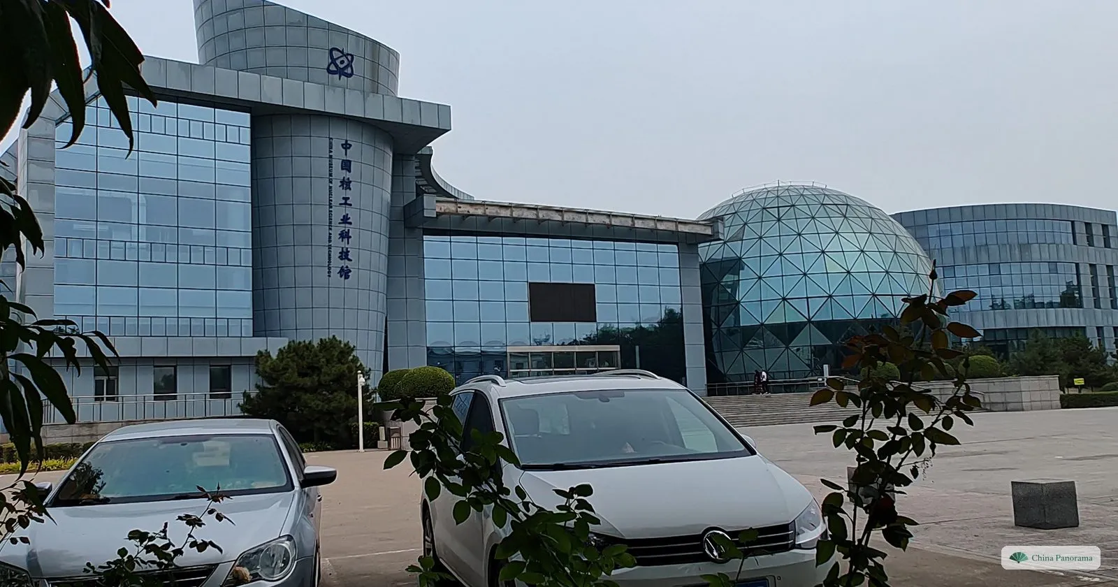 The glass and concrete building of the China Nuclear Industry Science and Technology Museum with a glass dome, and cars parked in front