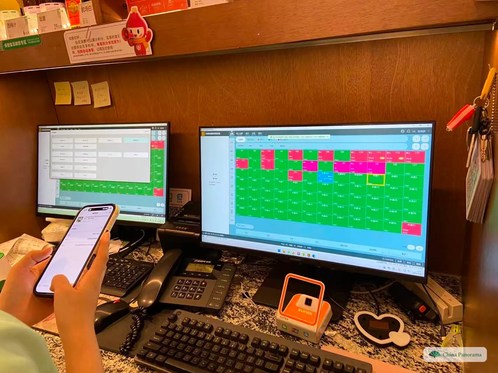 A restaurant till: a screen with a grid of numbered table squares in red and green, a keyboard, a phone, and an orange payment scanner