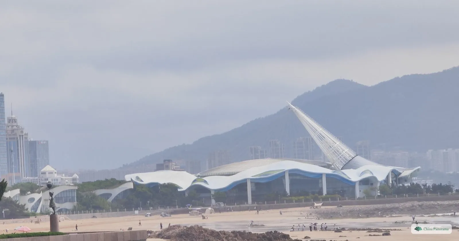 Shilaoren Beach in Qingdao with the white wave-shaped roof of the sculpture museum and the Laoshan ridge in the haze