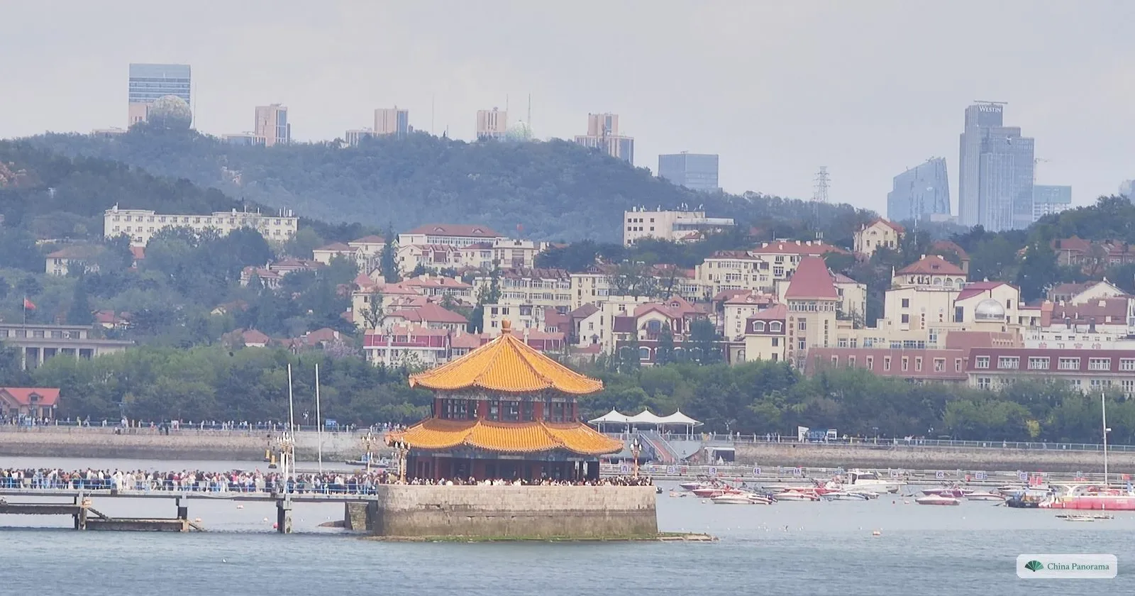 Zhanqiao Pier and the octagonal Huilan Pavilion in Qingdao Bay, with the red-roofed old town on the hill behind