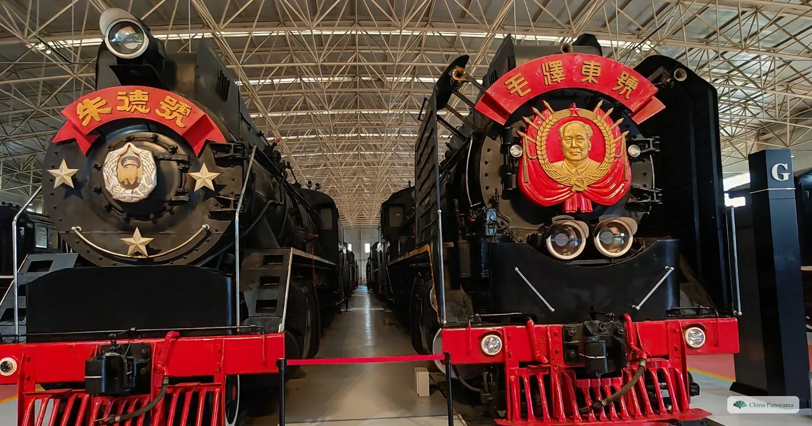Two black steam locomotives side by side in the China Railway Museum, their smokebox doors carrying red and gold emblems with the names Zhu De and Mao Zedong