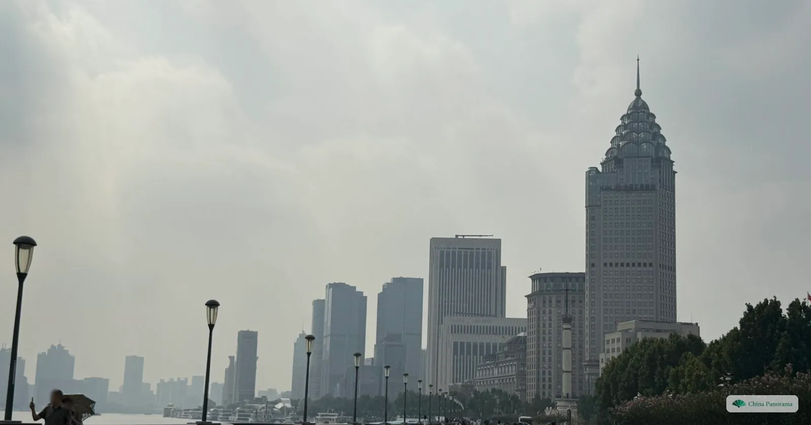 The wide, almost empty Bund promenade on a hazy morning, with lamp posts and the Bund Centre’s crown-topped tower ahead