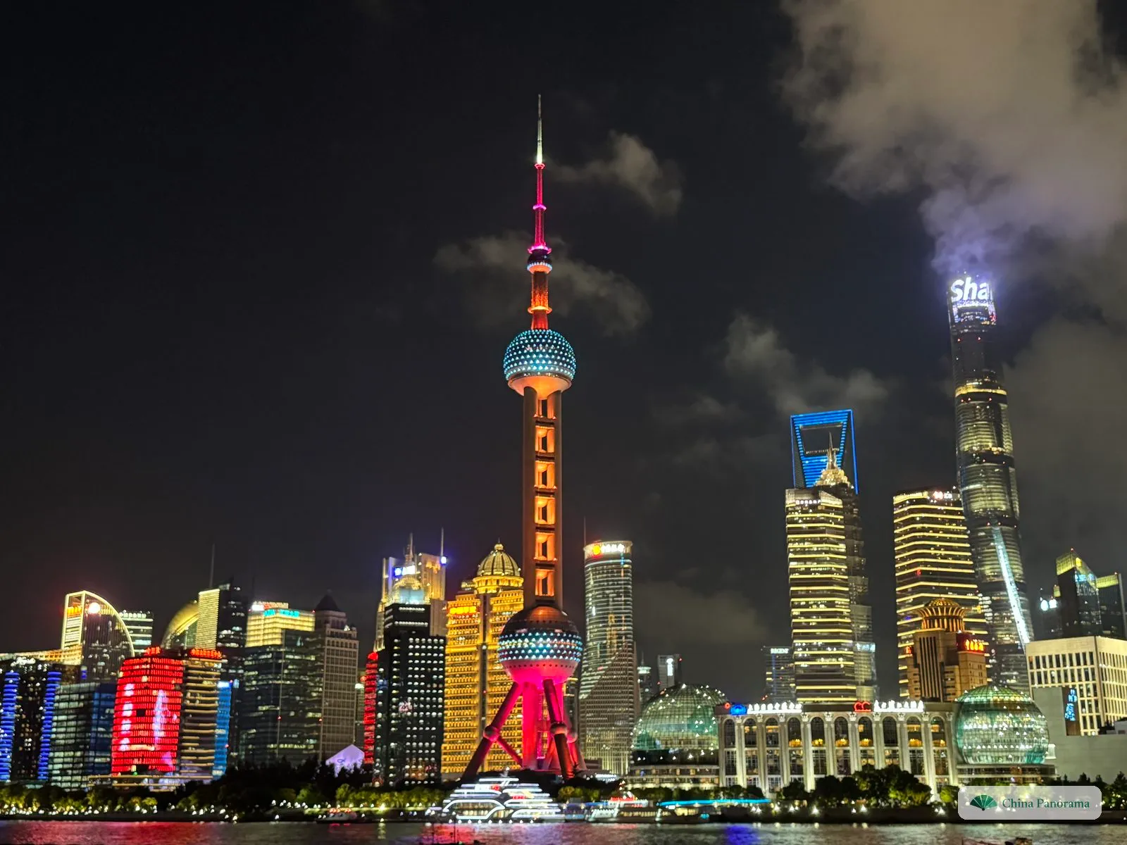 The Oriental Pearl Tower lit pink and orange in the middle of the Lujiazui skyline at night, with the Jin Mao Tower, the World Financial Center and the Shanghai Tower on the right and two glass globes along the river
