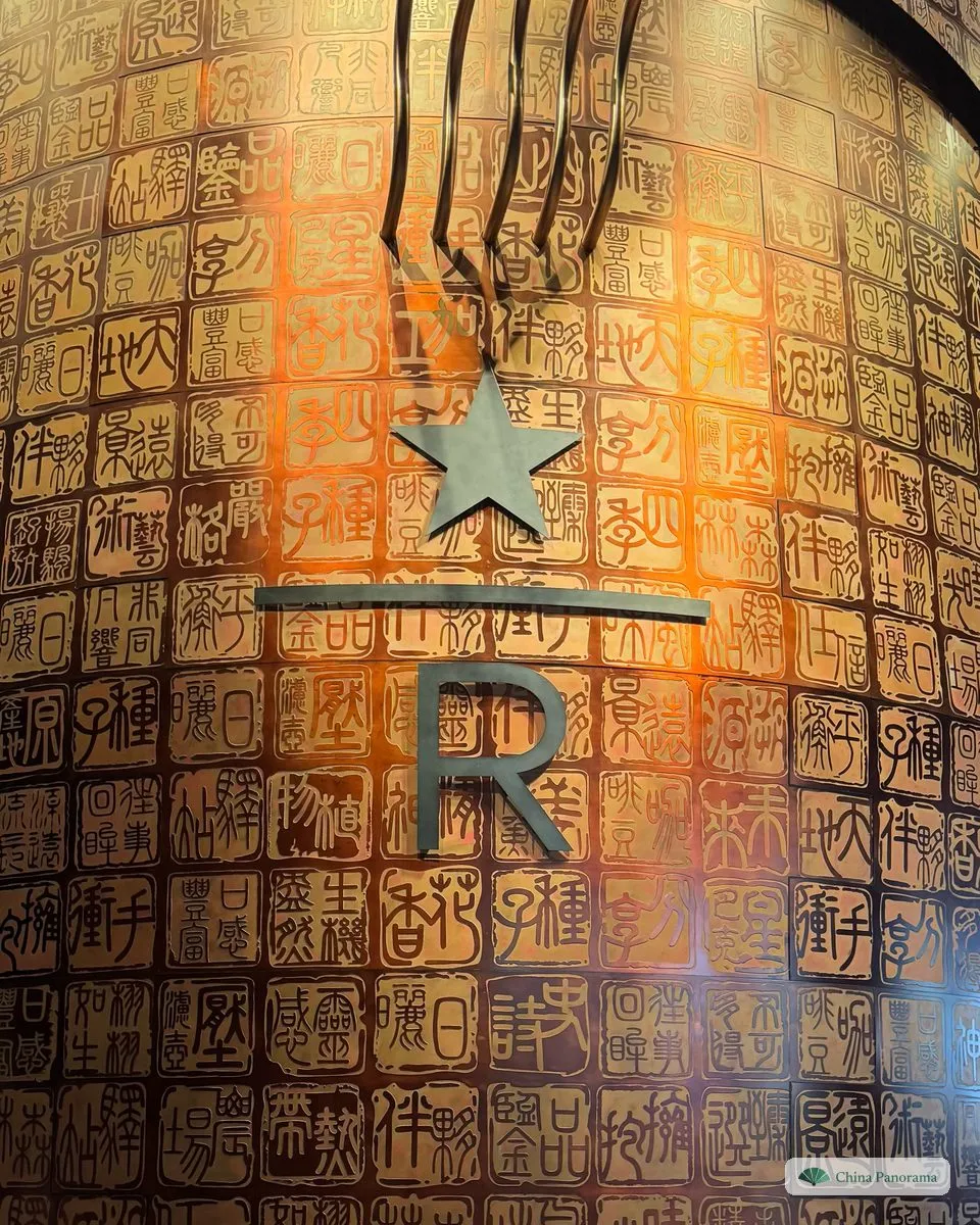 A tall copper cask covered in carved Chinese seal characters with the Starbucks Reserve star and a large R, lit warm orange