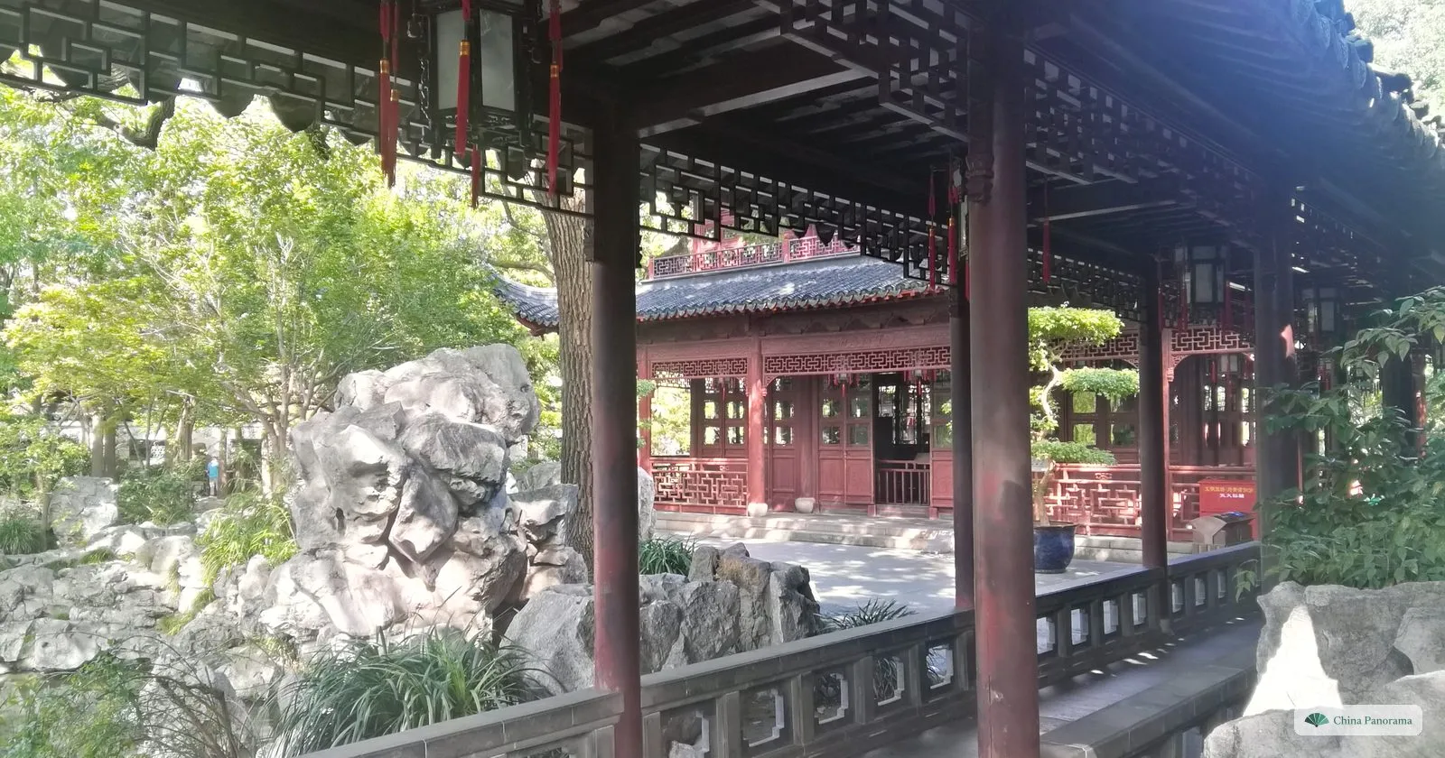 A covered walkway with red columns in Yu Garden, looking out on a rockery and another pavilion