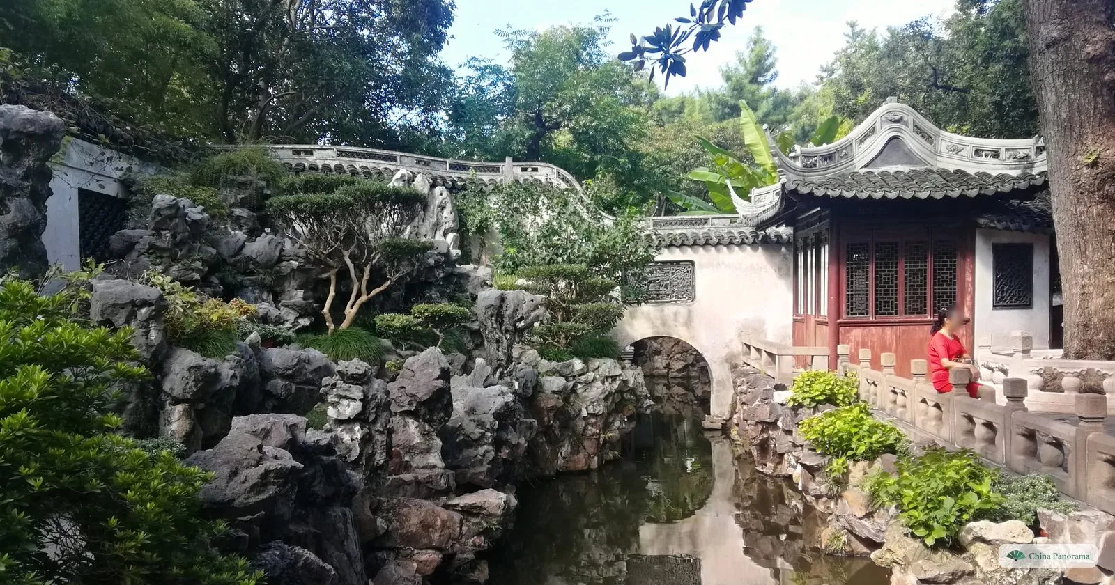 A rockery of grey limestone around a pond in Yu Garden, with a small pavilion and a stone bridge