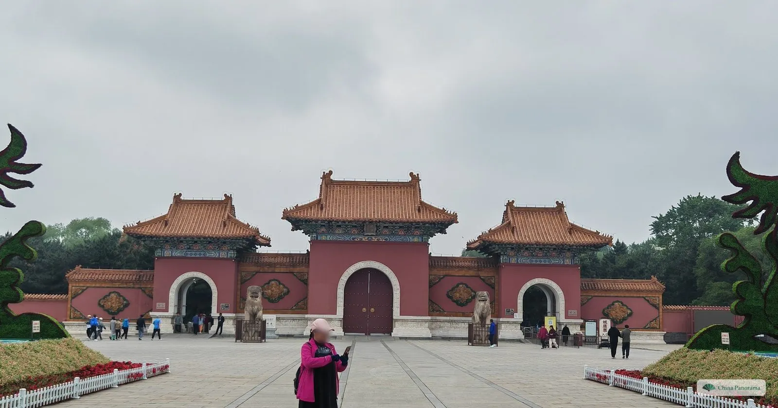 The red, three-arched main gate of Beiling Park with yellow-tiled roofs and stone lions, between two dragon-shaped hedges, early in the morning
