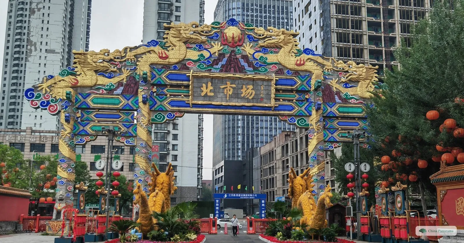 The painted Beishichang archway in Shenyang with golden dragons and lion statues, and tower blocks behind