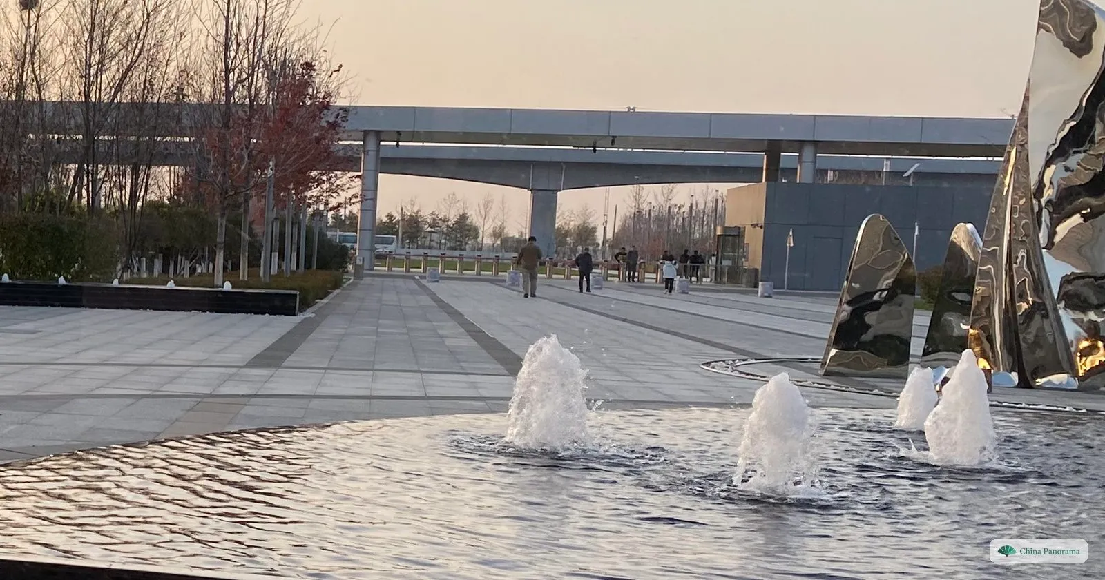 A pool with fountains and tall stainless-steel sculptures on the forecourt of BMW’s Tiexi plant in Shenyang, with an elevated walkway behind