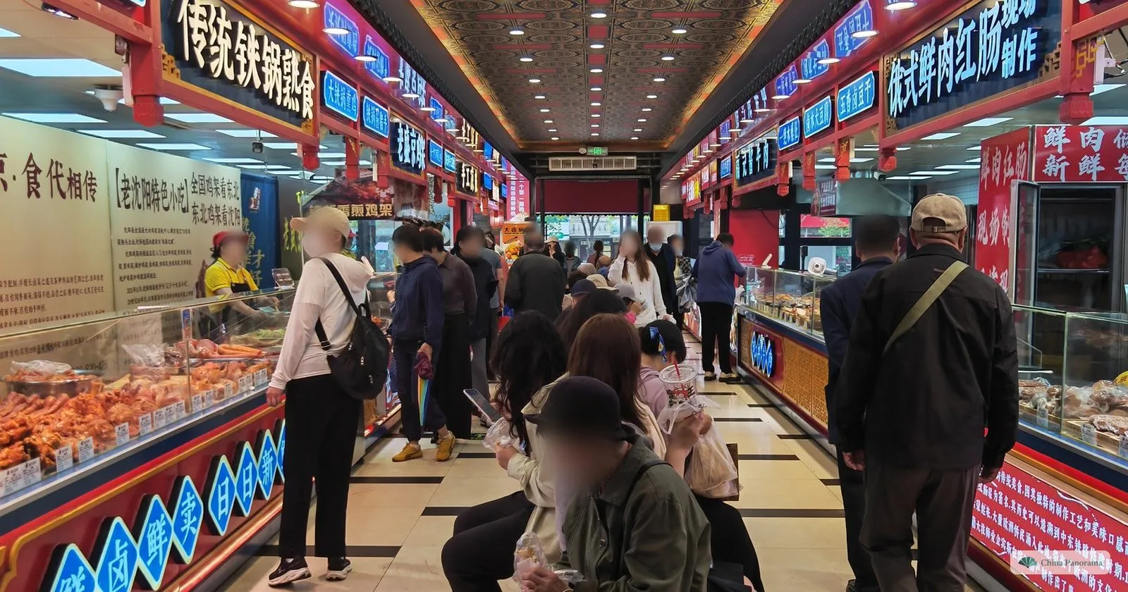 Glass counters of cooked meats and sausages inside the Dadongmen market, with shoppers in the aisle