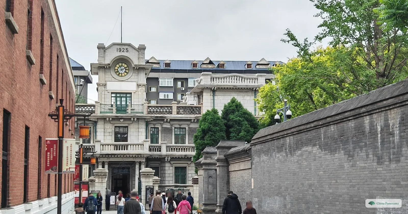 The pale stone clock tower of the former Frontier Bank, dated 1925, at the end of a lane between a red-brick building and the grey wall of Zhang’s Mansion