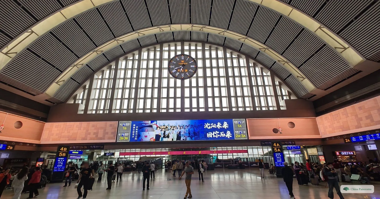 The arched waiting hall inside Shenyang Railway Station, with departure boards and travellers crossing the floor