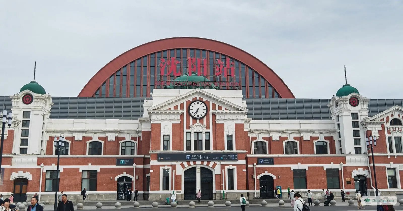 The red-brick front of Shenyang Railway Station, with a clock, two green domes and the arched roof of the modern hall rising behind it