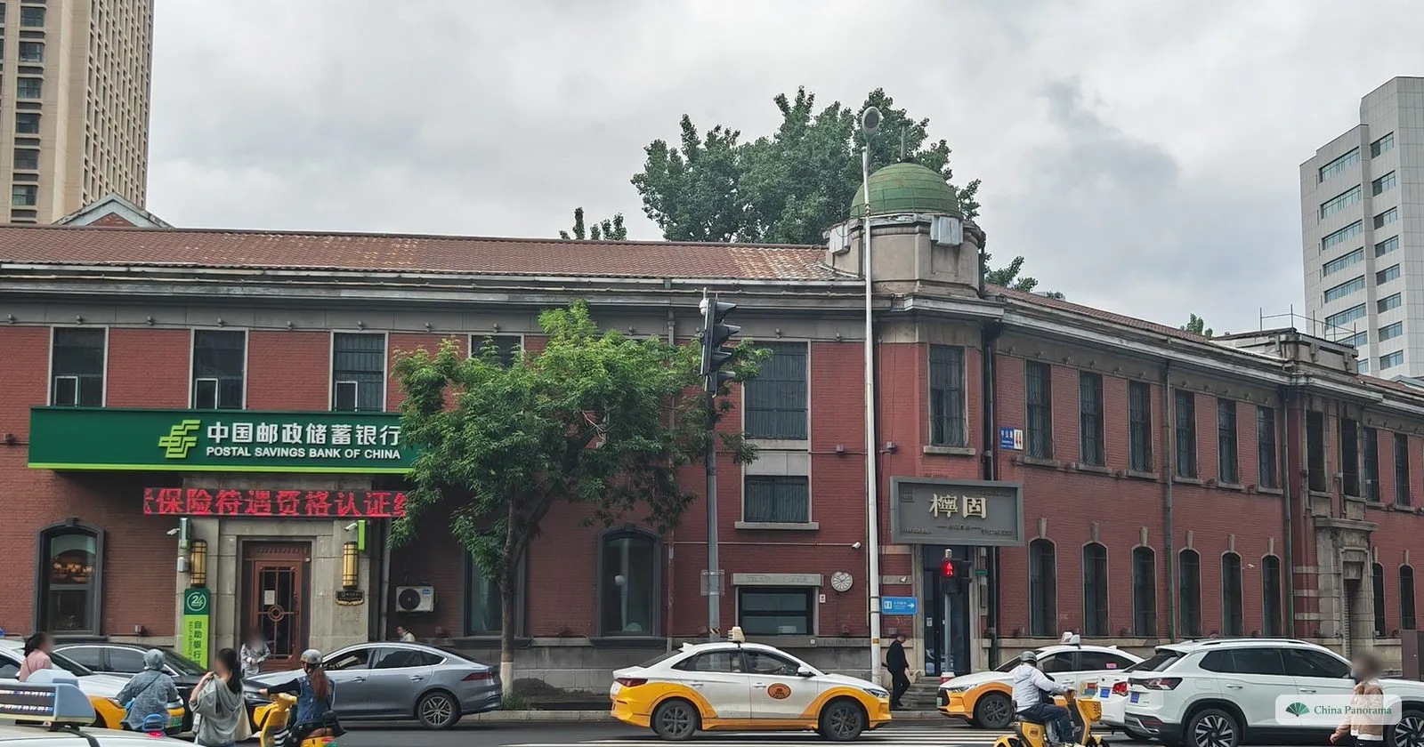 A long two-storey red-brick building with a small green dome near Taiyuan Street, with a Postal Savings Bank of China branch on the ground floor and taxis in front