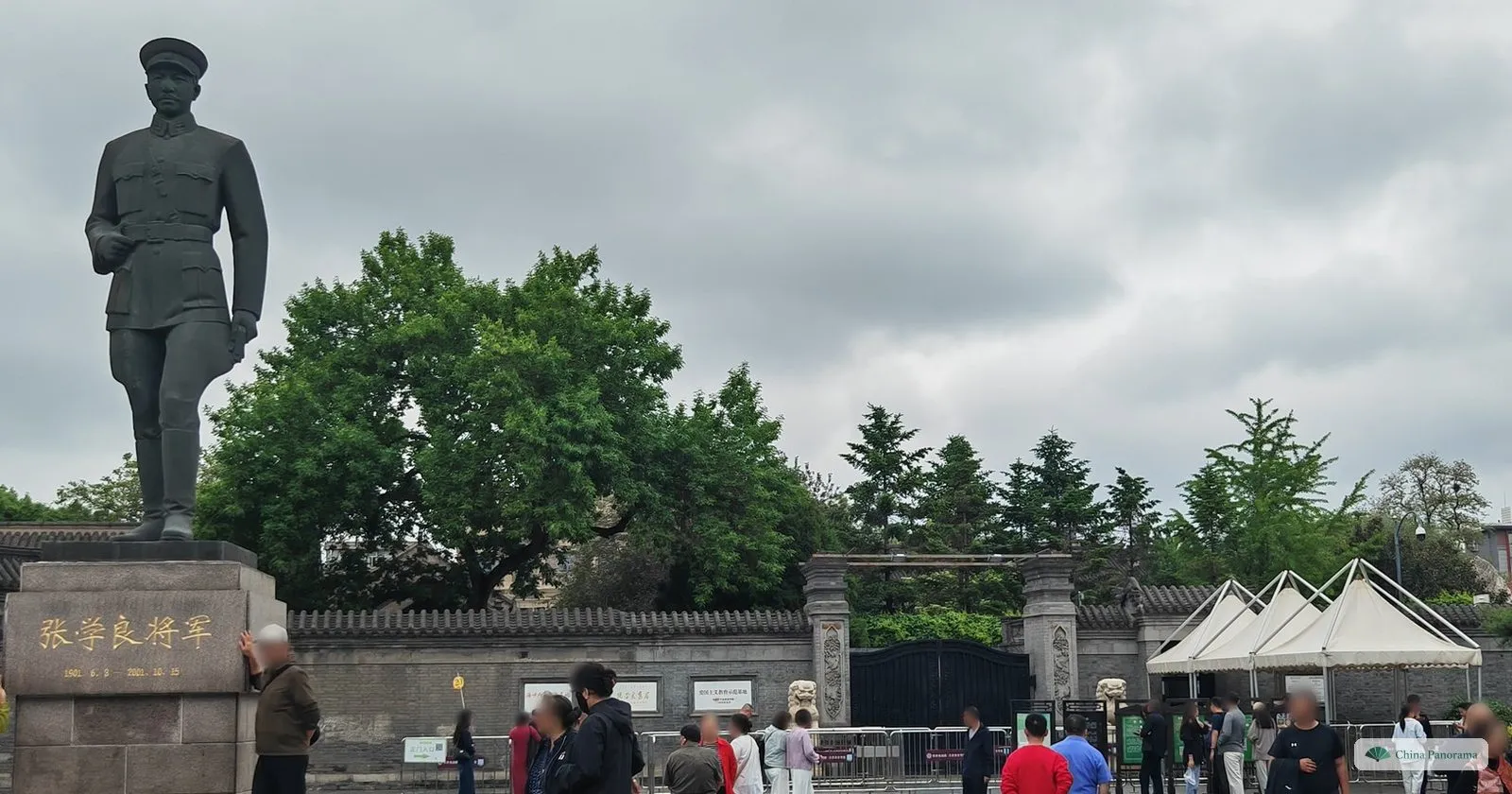 A statue of Zhang Xueliang in uniform on a plinth inscribed with his name and 1901–2001, in front of the grey entrance wall of Zhang’s Mansion