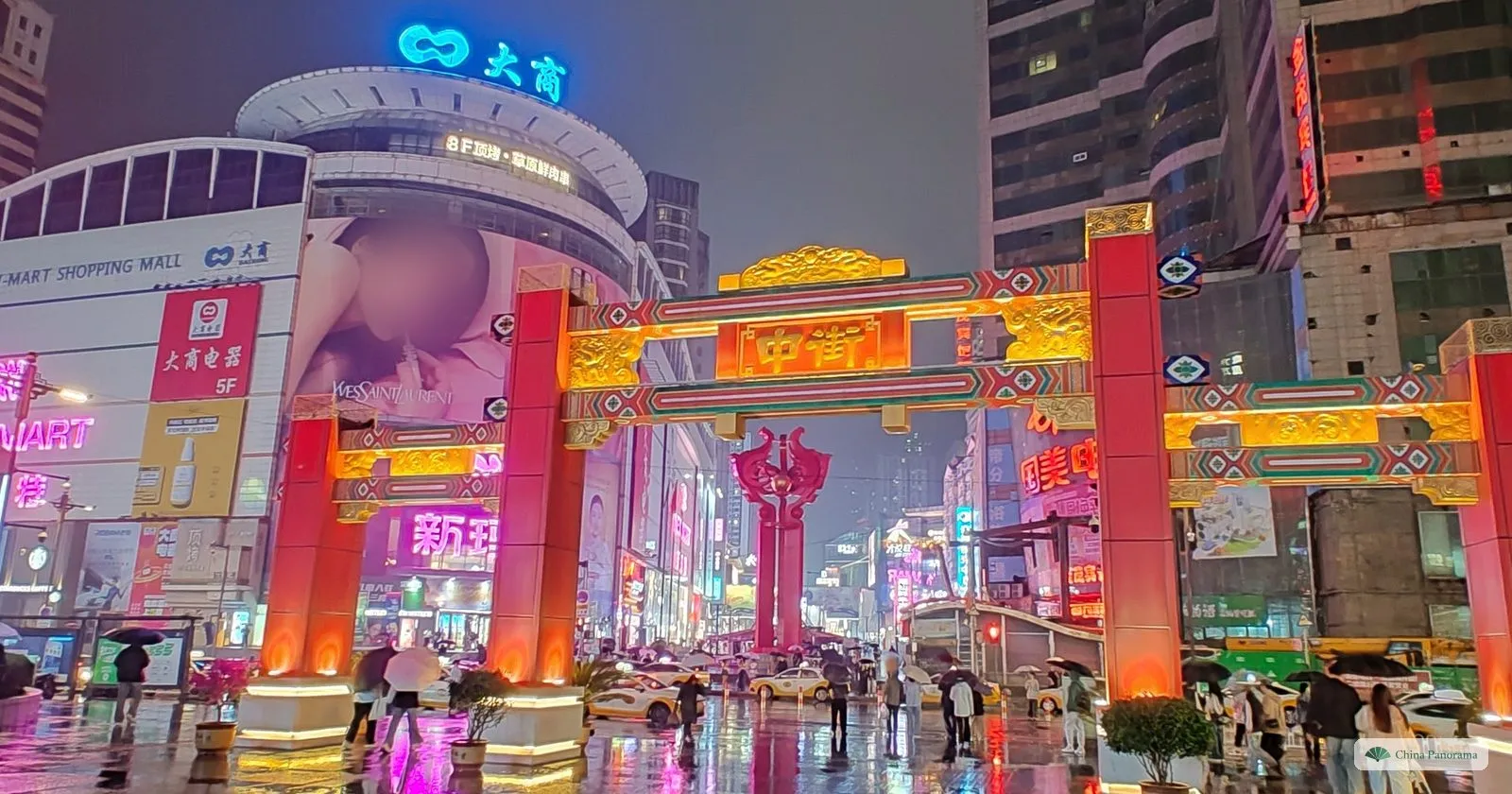 The illuminated red and gold archway over Zhongjie in Shenyang on a rainy night, with neon signs reflected on the wet pavement