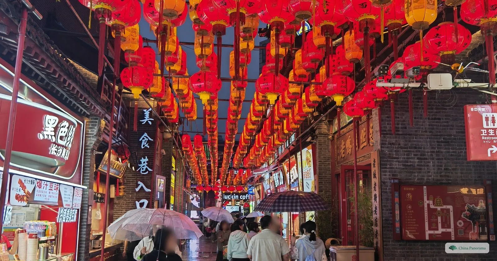 A food lane off Zhongjie hung with hundreds of red lanterns, with people under umbrellas in the rain