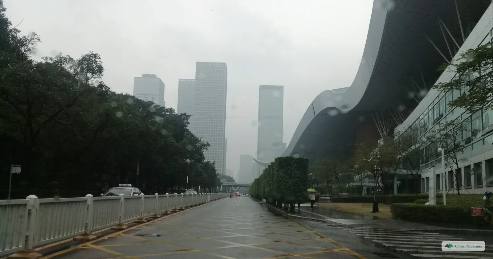 One end of the Civic Center roof sweeping up on the right, with an empty road and misty office towers in the rain ahead