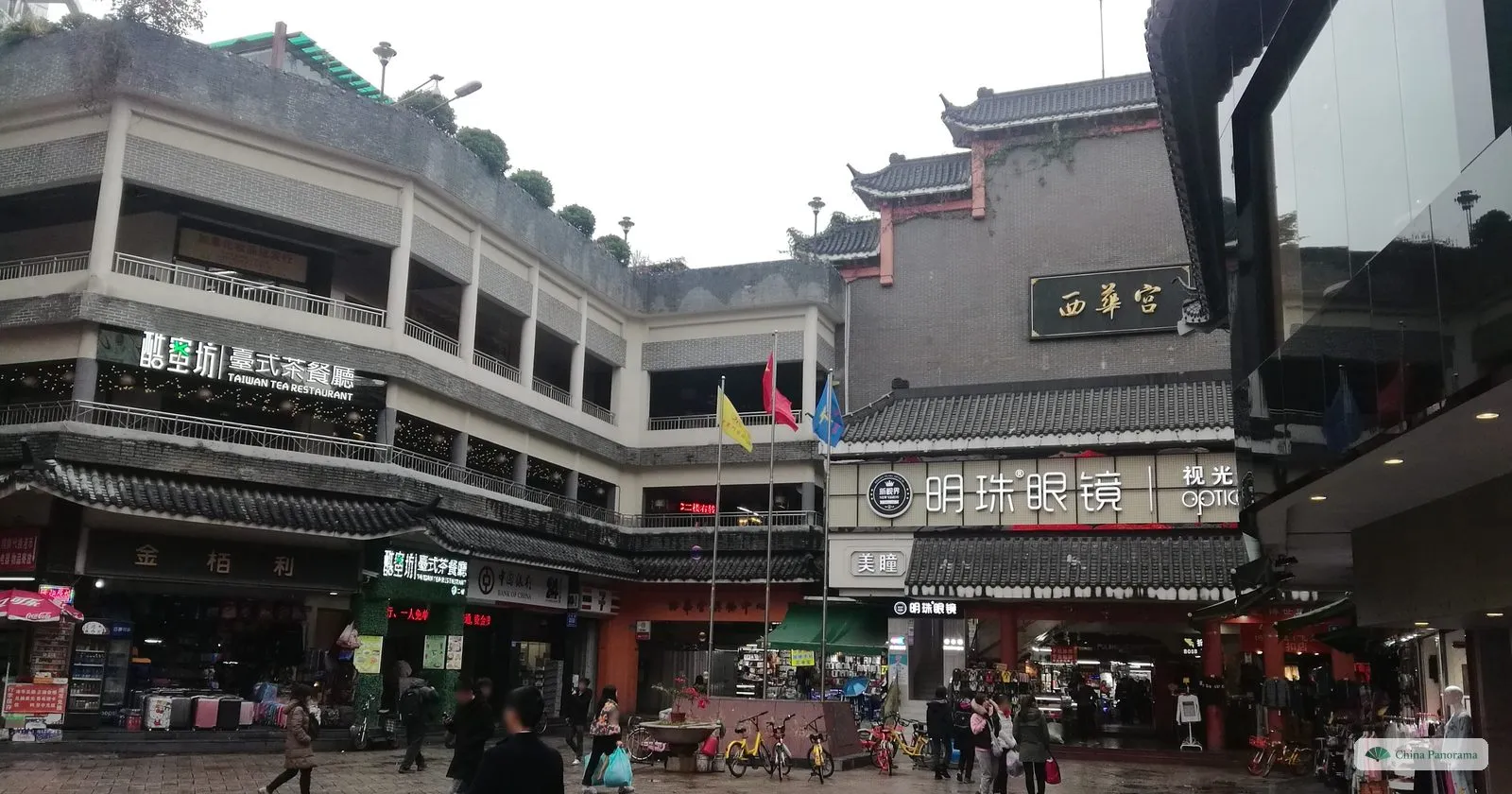Dongmen: a grey-walled building with upturned eaves and the gilded plaque 西华宫, next to a two-storey shopping arcade with a Taiwanese tea restaurant