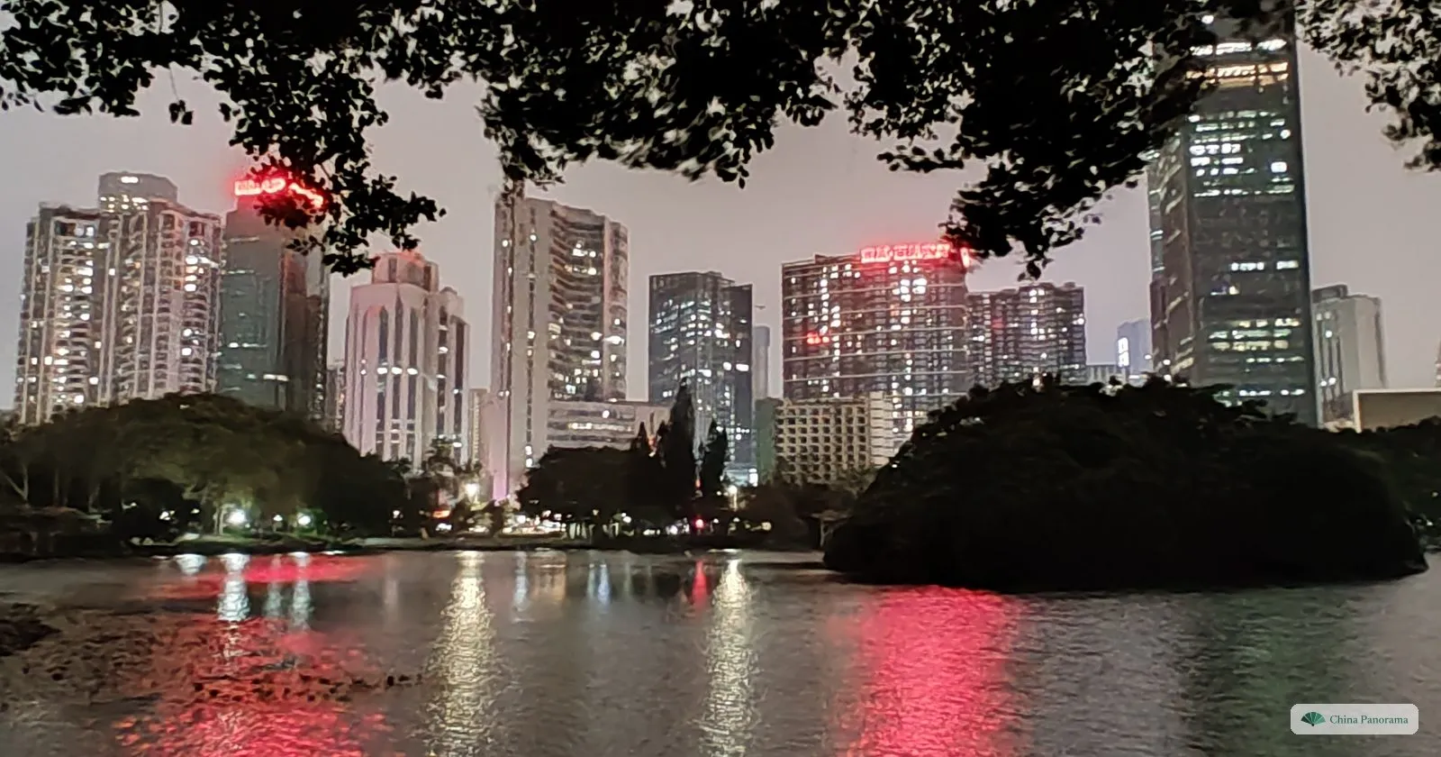 Lizhi Park after dark: the lake reflecting the red and white lights of the surrounding apartment towers, with a dark wooded island in front