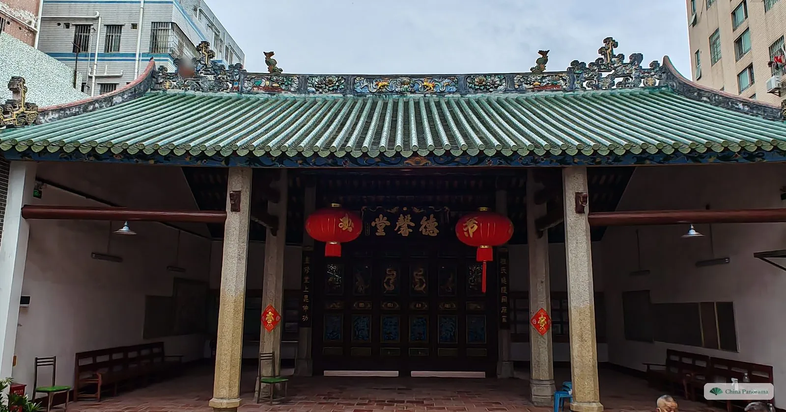 The open front hall of Dexin Hall in Nanyuan village, with green roof tiles, granite columns, red lanterns and the plaque 德馨堂 over carved inner doors
