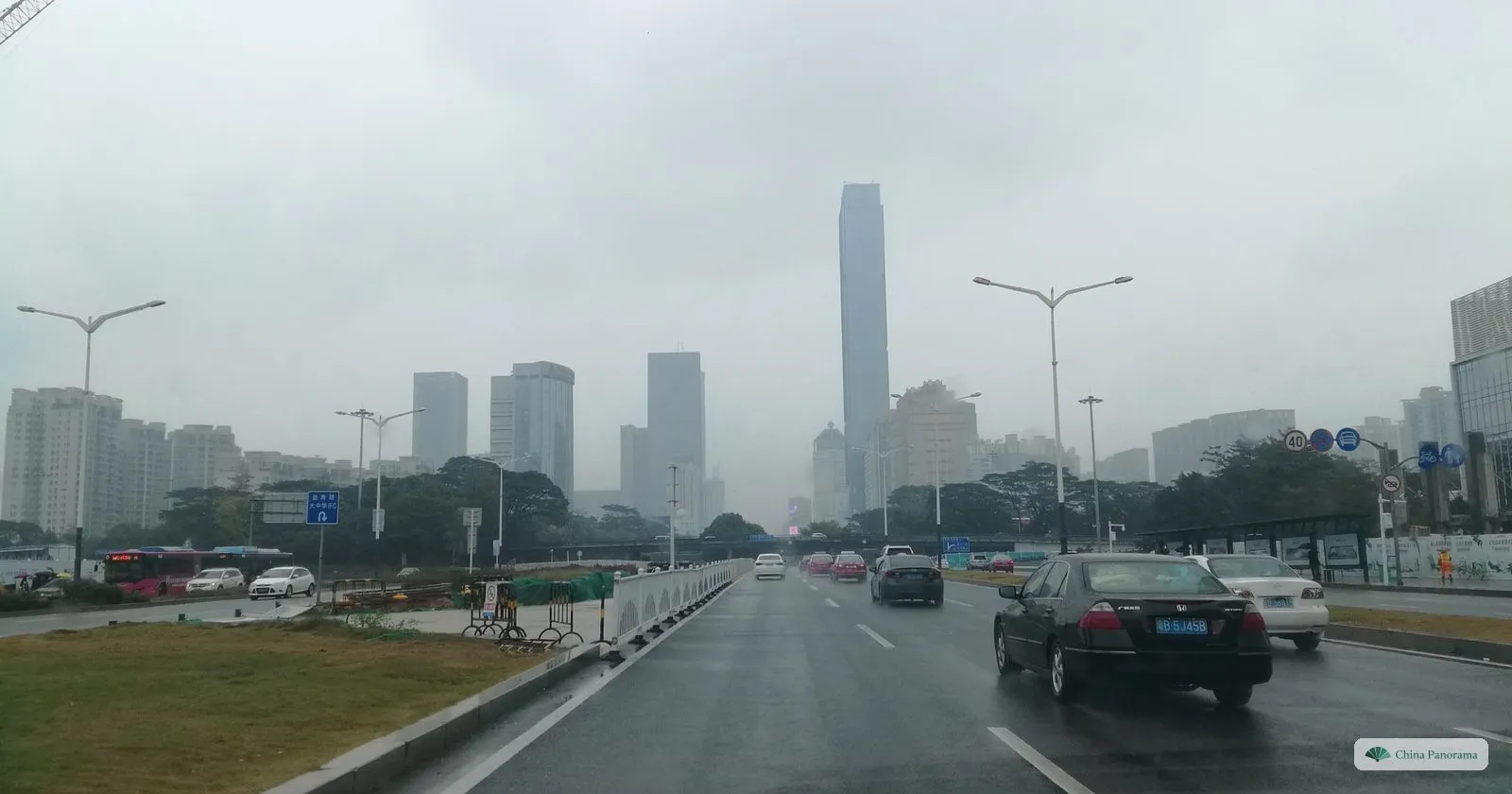 Shennan Boulevard in rain: a wide wet road with cars, a grass verge and a row of towers fading into mist, the tallest in the middle