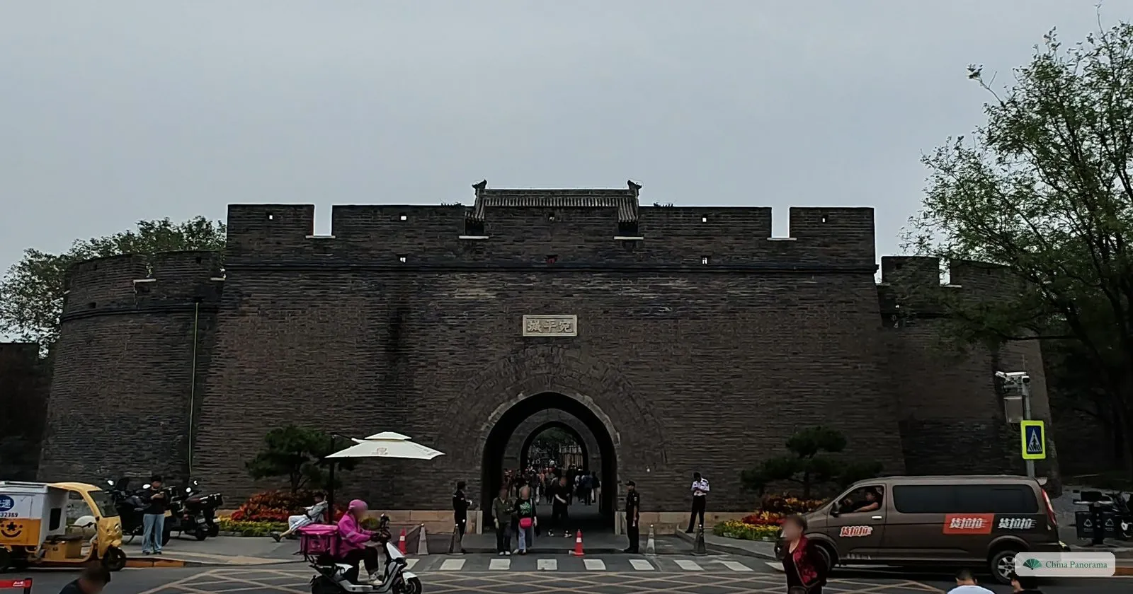 The grey brick wall and arched gate of Wanping fortress, with battlements along the top and traffic in front