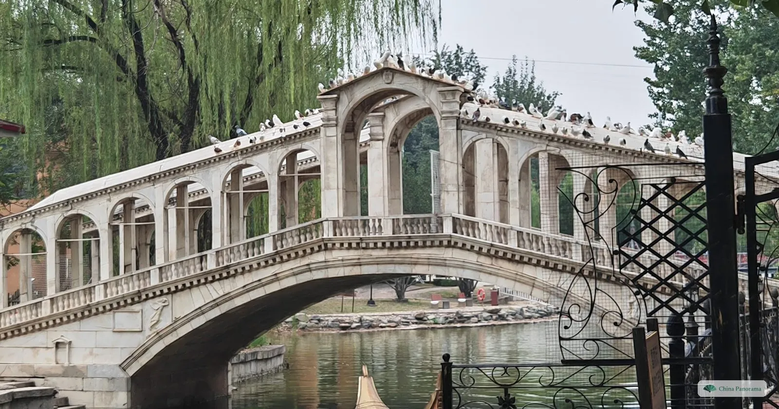 A scaled-down Rialto Bridge over a canal with a gondola in Beijing World Park, under willows