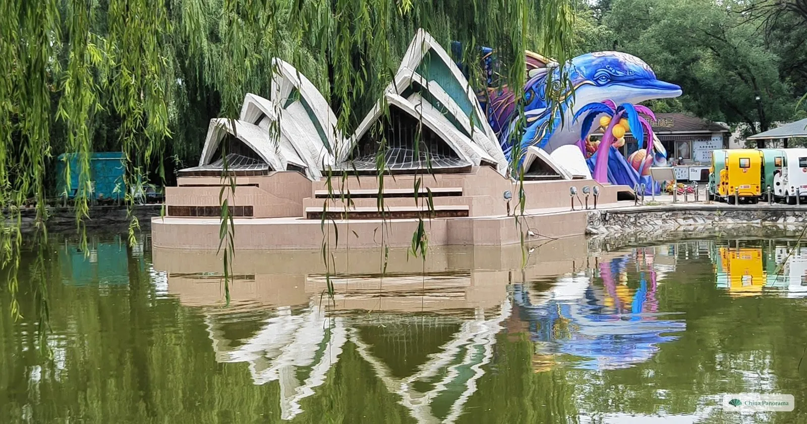 A miniature Sydney Opera House on a pond in Beijing World Park, reflected in the green water, with a lantern figure behind