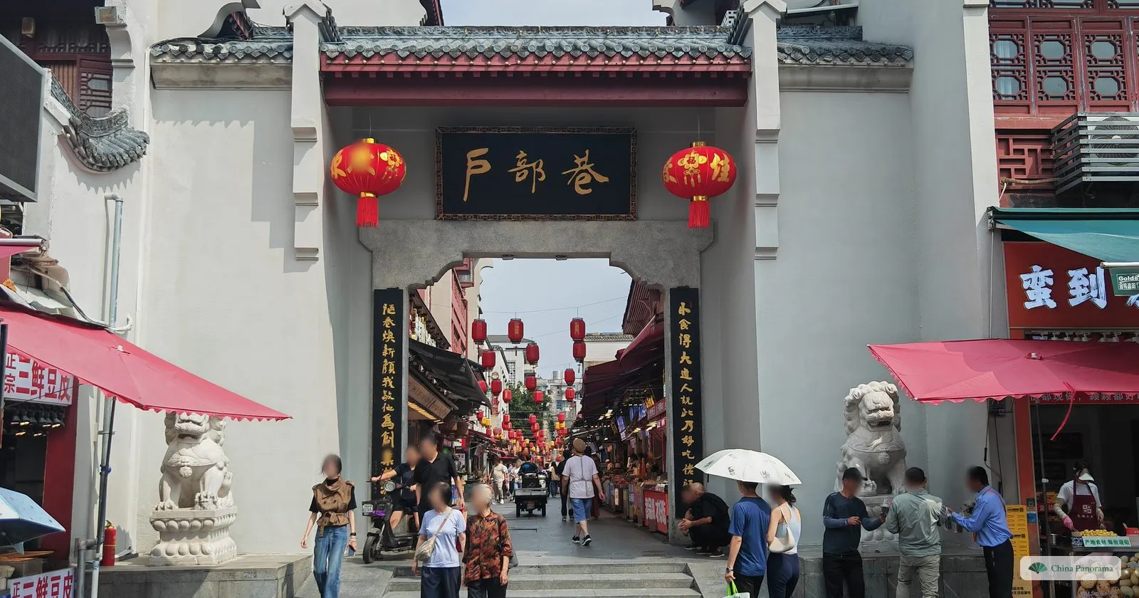 The white gate of Hubu Alley with a black plaque and red lanterns, a lane of snack stalls beyond