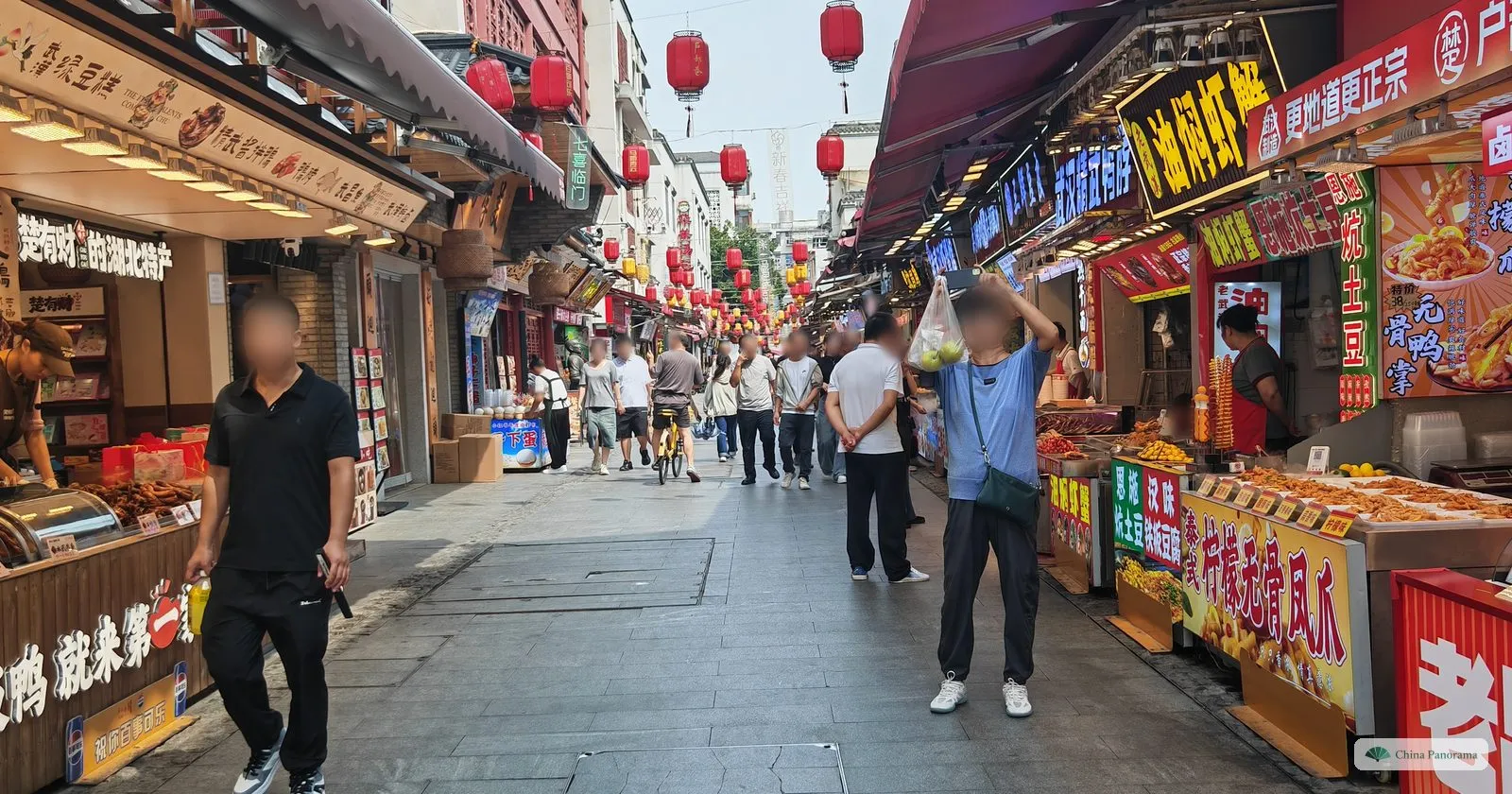 A busy pedestrian lane between snack stalls with bright signs, red lanterns hanging overhead