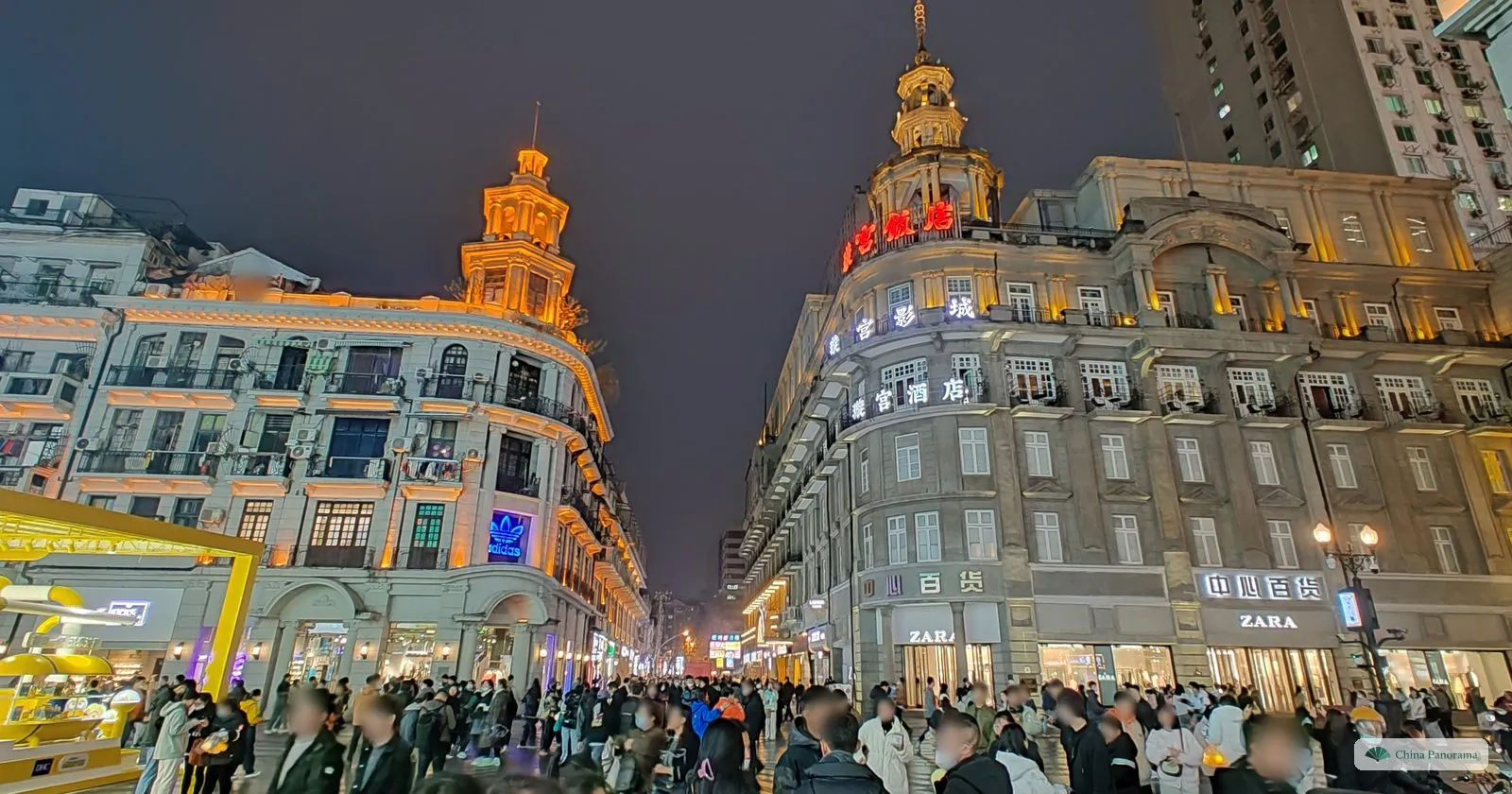 The Xuangong Hotel and another domed corner building lit up at night at the Jianghan Road crossing, crowds below