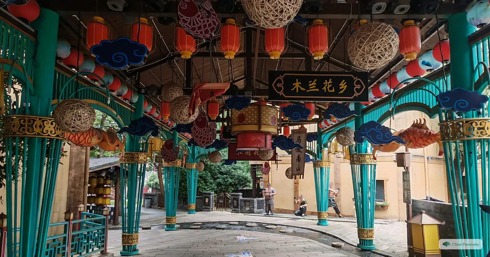 A covered arcade with turquoise columns hung with lanterns, paper fish and a sign 木兰花乡