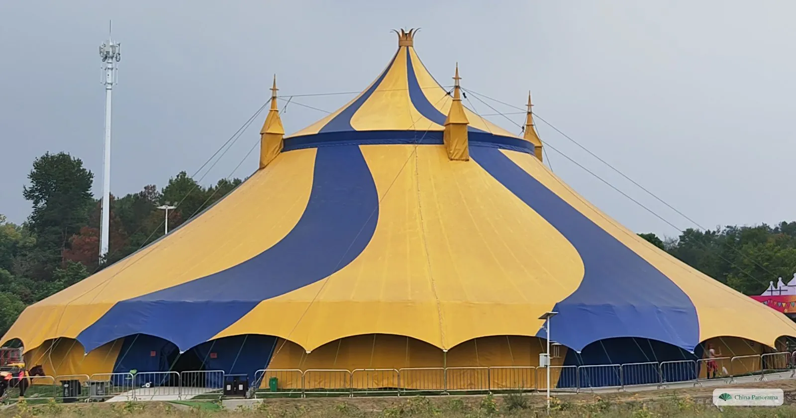A huge yellow and blue striped circus tent with pointed tops on a field