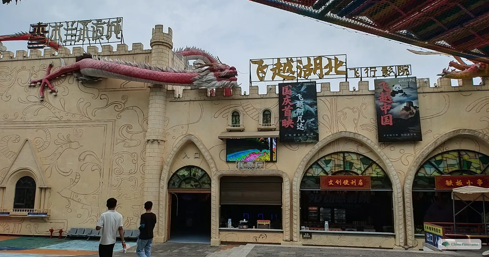 A cream-coloured mock castle with battlements, a red dragon sculpture along its wall and film posters, a flight-simulator cinema
