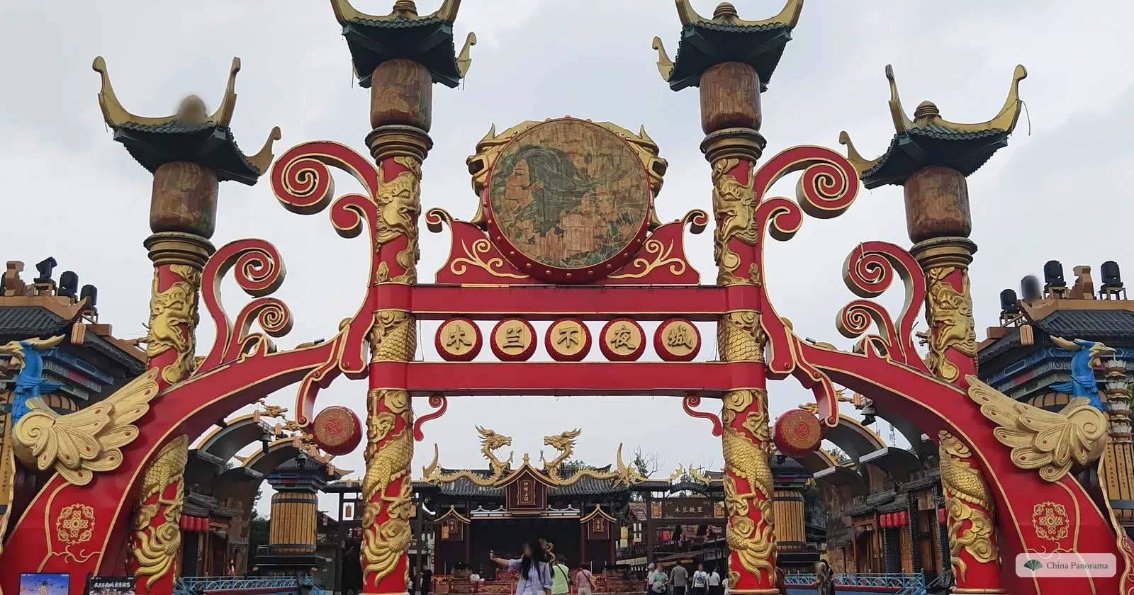 A huge red and gold gateway with dragon-carved columns and a round bronze disc, stages and dragon roofs beyond