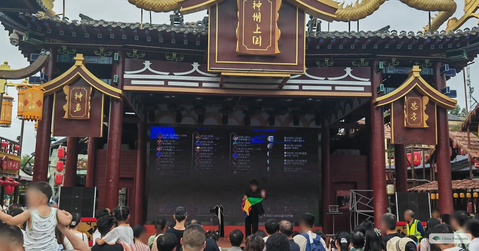 A crowd watching a performer on an ornate stage with a dark red roof and golden dragons