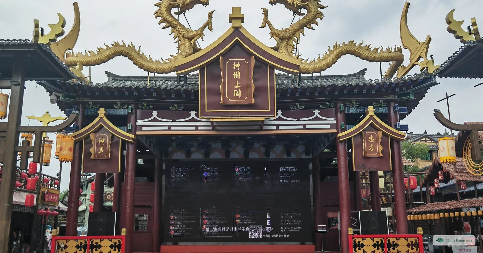 An open-air stage with dark red pillars, golden dragons on the roof and a big screen showing a programme