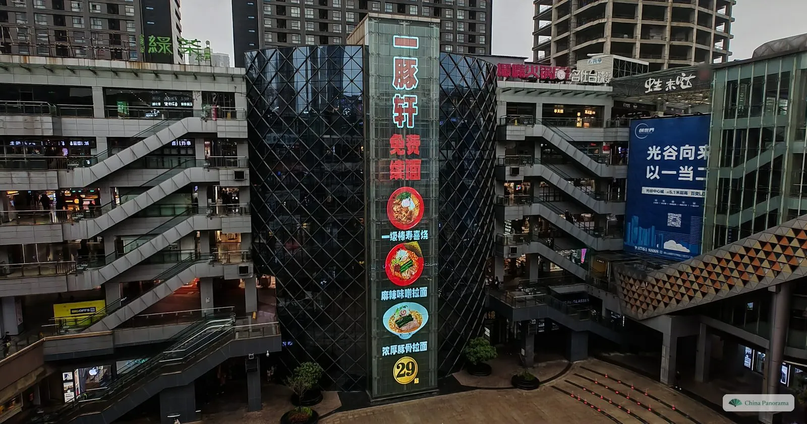 Criss-crossing escalators between shopping floors around a glass tower with a tall restaurant sign