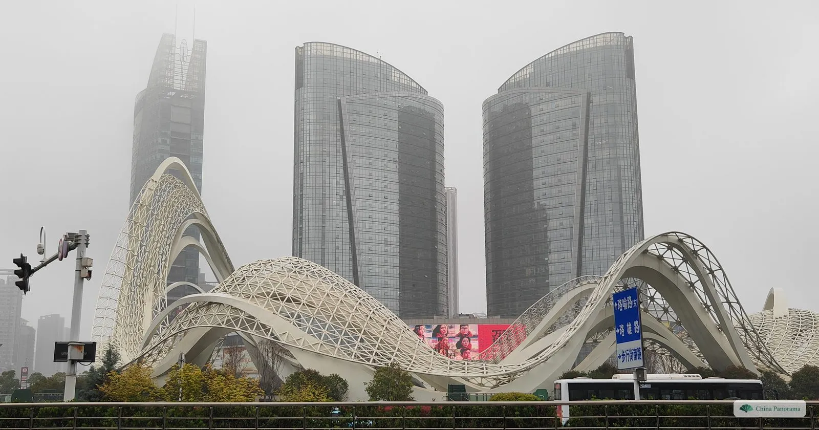 A white steel lattice sculpture of looping arches in front of two curved glass towers at Optics Valley Square