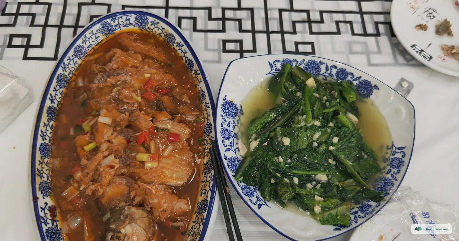 Two dishes on blue-and-white plates: a braised fish in red-brown sauce with chillies and spring onions, and stir-fried greens with garlic