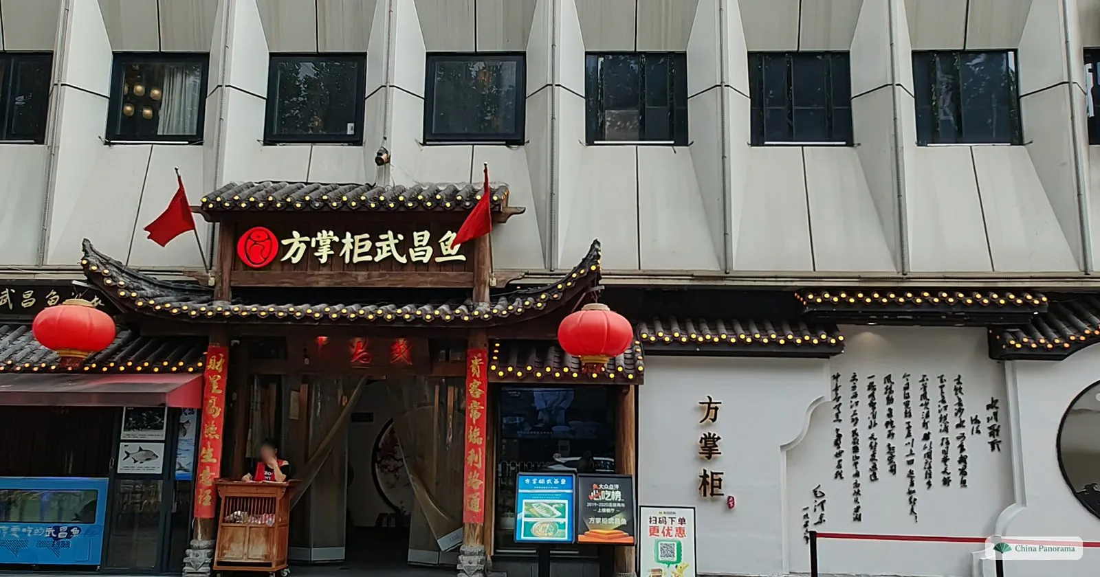 A restaurant front with a carved wooden canopy, red lanterns, a sign 方掌柜武昌鱼 and a white wall with calligraphy