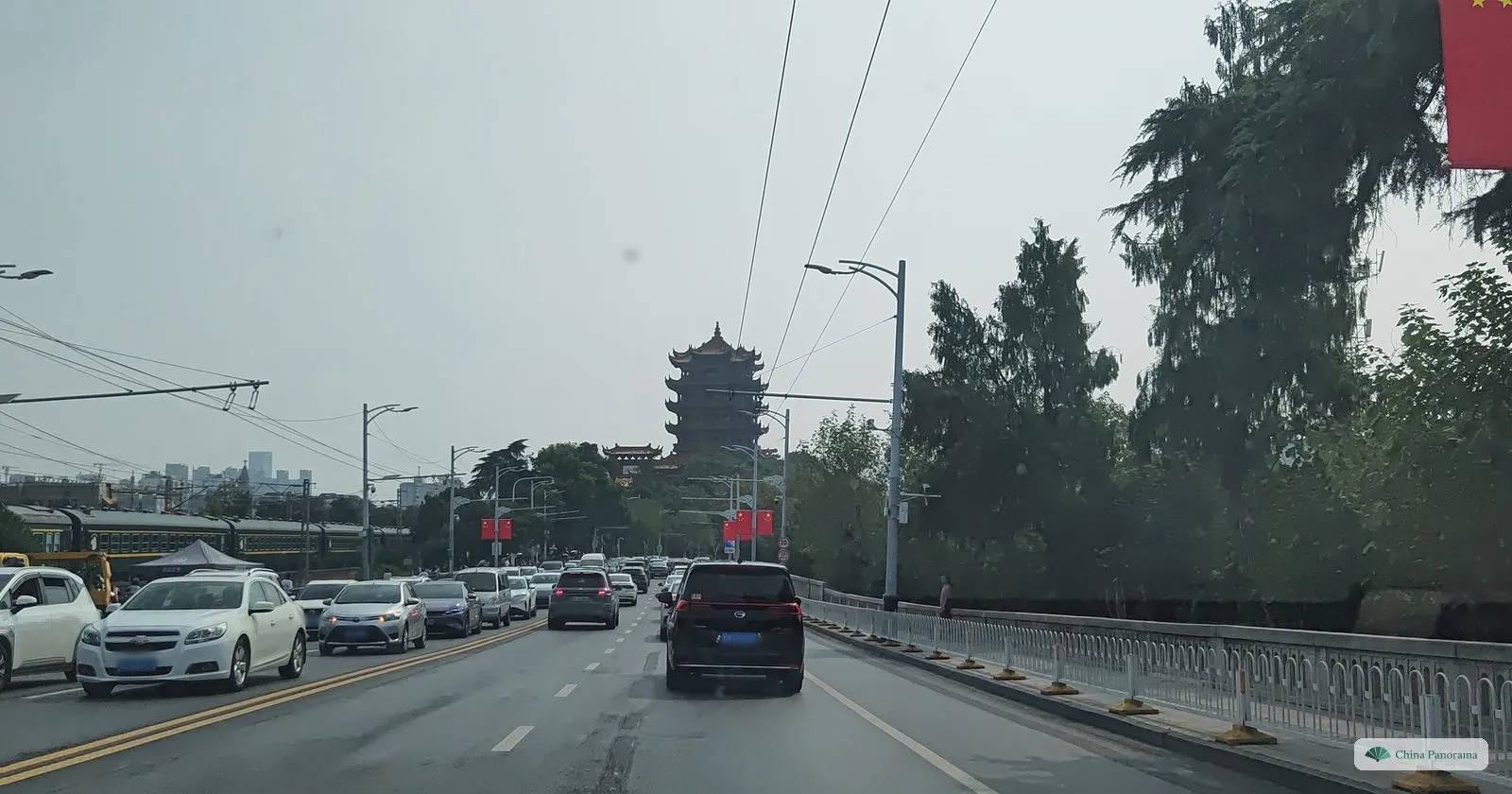 Through a windscreen: a road full of cars and, ahead on a wooded hill, a tall tower with many tiers of yellow roofs