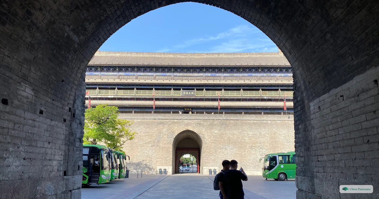 The East Gate tower of Xi’an framed by the dark brick arch of the barbican gateway, with two people photographing it from the shadow