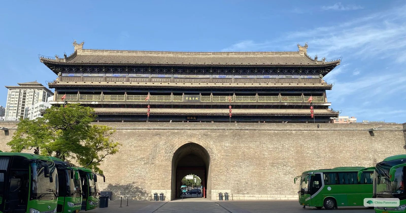 The gate tower of the East Gate of Xi’an, a long three-eaved wooden hall on top of the wall above an arched gateway, with green coaches parked in the courtyard in front