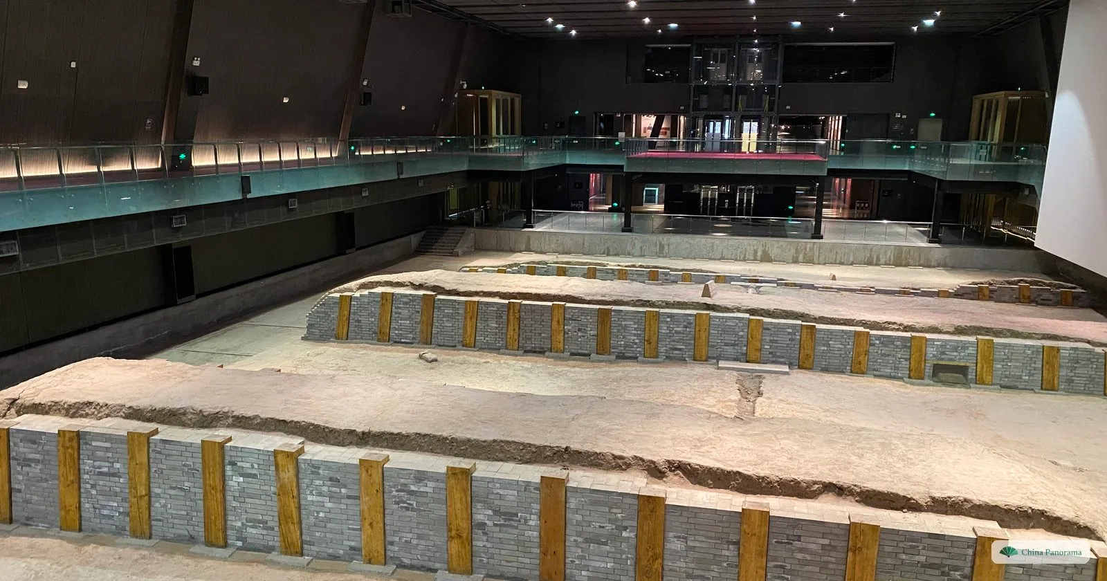 Excavated rammed-earth foundations, shored up with grey brick and timber posts, under the roof of a site museum at Daming Palace