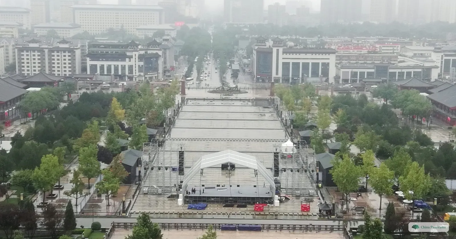 View north from the Giant Wild Goose Pagoda in the rain: the long stepped basin of the North Square fountain with a temporary stage on it, flanked by trees, and a straight road running on into the city