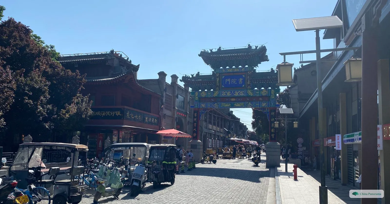 The painted archway at the entrance to Shuyuanmen, with the characters 書院門 on a blue plaque, grey-brick shopfronts and parked electric tricycles in front