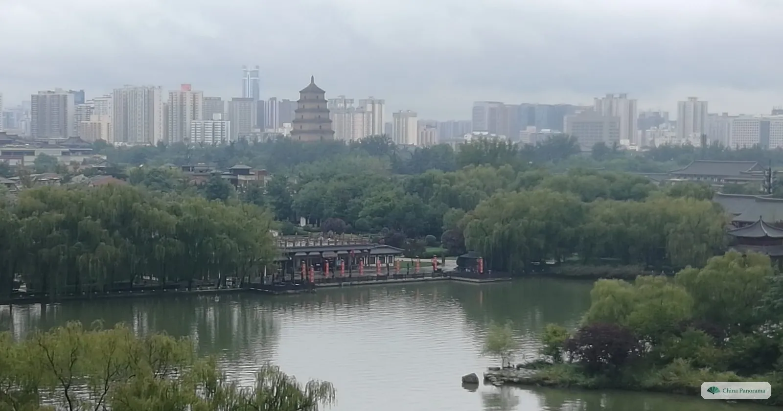 View across the lake of Tang Paradise from the Ziyun Tower to the Giant Wild Goose Pagoda, which stands in front of a line of apartment towers under a grey sky